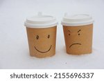 Small photo of Cups of coffee, on which a smile is drawn and in the eyes the sign of the ruble and chagrin. The cups are on the snow.
