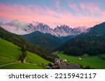 Val di Funes valley with amazing alpine Dolomites covered with pink clouds at sunset and Santa Maddalena village on the hill. 