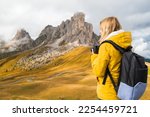 Professional photographer in yellow sport jacket takes pictures of Passo Giau pass using camera. Woman with backpack enjoys activity in Italian Alps 