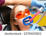 Small photo of Patient in protective glasses from UV light with tubule for liquid suction. Dentist puts tubule in woman mouth to work on teeth and cavity cure