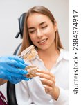 Small photo of A dentist, gloved and prepared, holds a human jaw model to elucidate a treatment approach to a patient