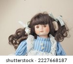 Vintage porcelain doll girl with brown eyes brunette with braided ribbons in a blue dress with white vertical stripes and a lace apron. 