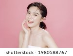 Asian woman has a lovely face is feeling happy with her perfect skin touch her face. She wears a white strapless bra. isolated over pink background. Skincare, cosmetology and plastic surgery concept.