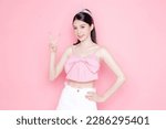 Small photo of Cute Asian woman model gathered in ponytail with korean makeup style on face have plump lips and clean fresh skin wearing pink camisole show V sign on isolated pink background.