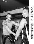 Small photo of personal trainer helping young man making pulley pushdown standing - tricep exercise - finish exercise - focus on the trainer left eye