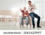 Small photo of Did you see. Happy unshaken senior man sitting on the chair with a son pointing aside and laughing.