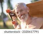 Smiling mature man holding longboard in a city park.