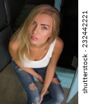 Small photo of Beautiful stylish daring hussy blond girl with straight hair in white T shirt and jeans confidently proudly looking at camera sitting in old peeling blue cupboard top view waist up