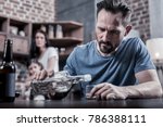 Drinking father. Serious unhappy sad man sitting at the table and pouring vodka into his glass while having alcohol addiction