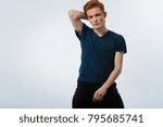 Small photo of Sporty. Attractive humourless red-headed young man sitting on the chair and staring and having his hand on his nape