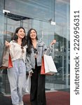 Small photo of Portrait, Two joyful and attractive young Asian female friends walking out of the shopping mall with their shopping bags, had a fun shopping time together.