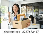 Small photo of Smiling and excited young Asian female office worker is celebrating her resignation, carrying her personal stuff, happy to leave her job or change job positions.