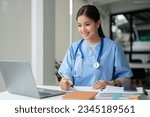 Small photo of A beautiful and professional Asian female doctor is working on her medical cases on her laptop or making a video call medical consultation with a patient while sitting in her office.