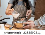 Close-up image of a couple mixing pancake flour and pouring milk into a mixing bowl while making pancakes in a lovely minimalist kitchen together. Couple and leisure concepts