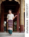 Small photo of A charming Thai-Asian woman in a traditional Thai-Northern dress with a garland in her hand is walking down the stairs of a temple, visiting a temple on a Buddhist holy day. Thai culture