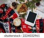 Winter cozy composition with cup of coffee, warm sweater, piece of apple pie, jars with lights and e-book with copy space and autumn leaves. Christmas morning. Hygge home interior.