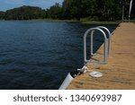 A dock at a lake with a ladder and a cleat tied with a dock line which looks inviting  for a swim.