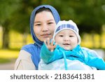 Small photo of Cute young islamic kazakh woman hugging, playing with her little son, newborn boy. Yappy asian mother in hijab holding baby in hands outdoors. Family concept