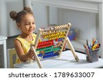 an african-american girl sits at a table and counts on an abacus and smiles