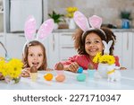 Small photo of Two girls with Bunny ears on her heads is happy find a chokolate eggs after Easter egg hunt.