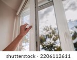 One sided open window. A hand opens a vinyl plastic window on a blue sky background.