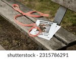 Small photo of An orange collar with a leash and a flyer about a lost dog lie on a park bench. Lost dog. the concept of love for pets.