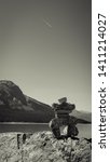 Small photo of A Handmade Inukshuk/Rock-Stack sits lake and mountainside. As jetstream streaks above in the vast sky. Located Lake Abraham.