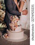 Small photo of White three tier wedding cake. Vanilla sponge cake, cream cheese cream. The cake is decorated with pink and red roses and green leaves. wedding. Bride and groom