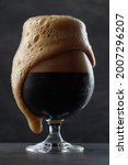 Small photo of Detail of dark beer with overflowing foam head. Stream of dark stout pours into a beer glass. Selective focus