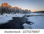 Half frozen River Juutuanjoki with rapids in winter at sunset under rising moon, Inari, Lappland, Finland