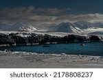 SNOW COVERED MOUNTAINS AND ICE SHELF WITH SOME EXPOSED ROCK IN A INLET WITH SEVERAL ZODIACS NEAR THE ISLAND OF SVALBARD NORWAY IN THE ARCTIC