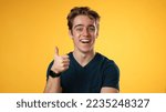 Small photo of Portrait of confident young man 20s with smiling crossing arms nod head yes, giving thumbs up, posing isolated on yellow background studio. People lifestyle emotions concept.
