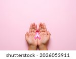 Woman hands holding pink ribbon over pink background, breast cancer awareness, October pink concept