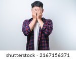 Asian young man wearing casual shirt with sad expression covering face with hands while crying. depression concept over white background