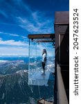 Small photo of Chamonix, France - July 10, 2021. Tourist stands in the 'Step into the Void' glass box on the Aiguille Du Midi (3842m) mountain top above Chamonix, Mont-Blanc massif, Haute Savoie, France.