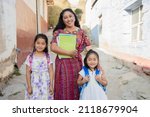 Small photo of Hispanic mom and daughters ready to go to school - Latin mom accompanying her daughters to school - Hispanic girls with backpack outside their house in rural area