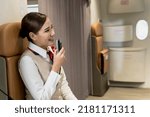 Small photo of Portrait young female Asian cabin crew using announcing phone on board, woman flight attendant holding microphone to annouce welcome on board, female air hostess greeting passengers on plane
