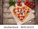 Pizza heart shaped with pepperoni, tomatoes, mozzarella, garlic and parsley on vintage wooden table background. Concept of romantic love for Valentines Day.