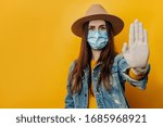 Small photo of Serious traveler tourist woman in medical sterile face mask gloves, showing stop gesture, trying to settle down conflict while pandemic coronavirus, isolated on yellow background. Quarantine concept