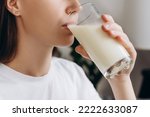 Cropped shot healthy young woman drinking milk with calcium for strong bone at home. Calm brunette girl holding soy milk on glass enjoy with nutrition wellness life. Natural milk fresh concept