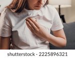 Young unhealthy female sit on couch having difficulty breathing pain of heart, touches his chest with hand. Trouble breathing, chest pain. Heart attack, thoracic osteochondrosis, panic attack concept