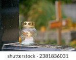 Small photo of Candle (snitch) on a black tombstone in a cemetery during the day in Hungary. All Saints' Day, copy space. Wooden cross in the background.