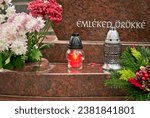 Small photo of Candle (snitch) on a tombstone in a cemetery during the day in Hungary with a Hungarian sign " Emleked orokke" which means "Your memory forever". All Saints' Day.