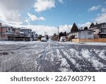 Small photo of Slushy residential street after snow storm or arctic blast. Sunny day with big melt down on unplowed side street with parked cars. East Vancouver with skyline of downtown Vancouver. Selective focus.