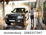 A man washes his car during the day, washes of the foam. A black SUV car at a self-service car wash. Washing the car with your own hands. A black auto in cleaning foam. 