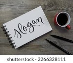 Small photo of SLOGAN lettering in notepad with cup of coffee and pens