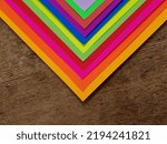 Small photo of Striped multi-colored "triangle" of multi-colored sheets of paper, in the sun, on a wooden table (macro, angle of sheets superimposed on each other, full face, texture).