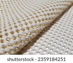 Small photo of Light yellow, rubberized, mesh, anti-slip carpet underlay - on a white background, with a diagonal fold (macro, texture).