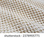 Small photo of Wavy light yellow, rubberized, mesh, anti-slip carpet underlay - on a beige background, in diagonal folds (macro, texture).