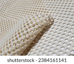 Small photo of Light yellow, rubberized, mesh, anti-slip carpet underlay - on a white background, with a rounded fold (macro, the edge of the material, texture).